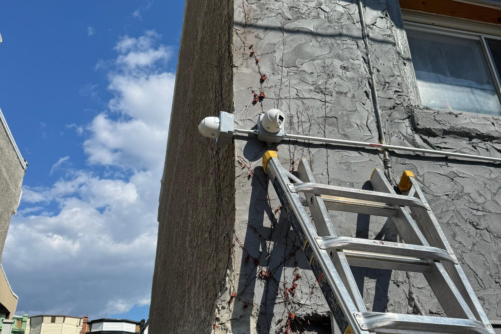Two security cameras installed on the corner of a New Jersey home, with the installer's ladder still leaning against the wall